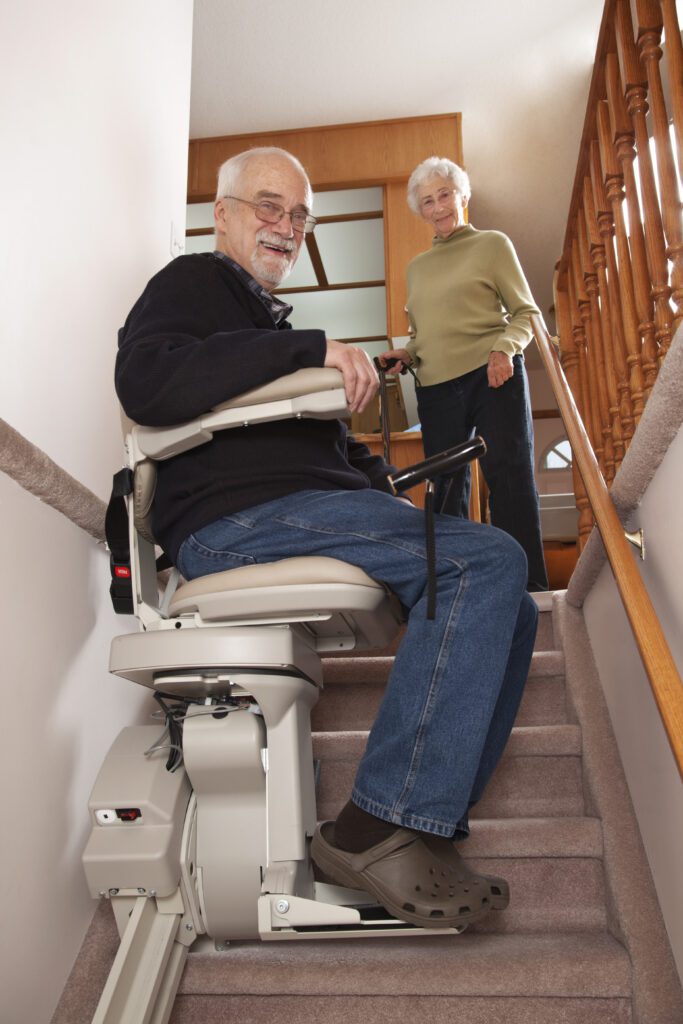 older man on seat of stair lift in Delaware; older woman behind him