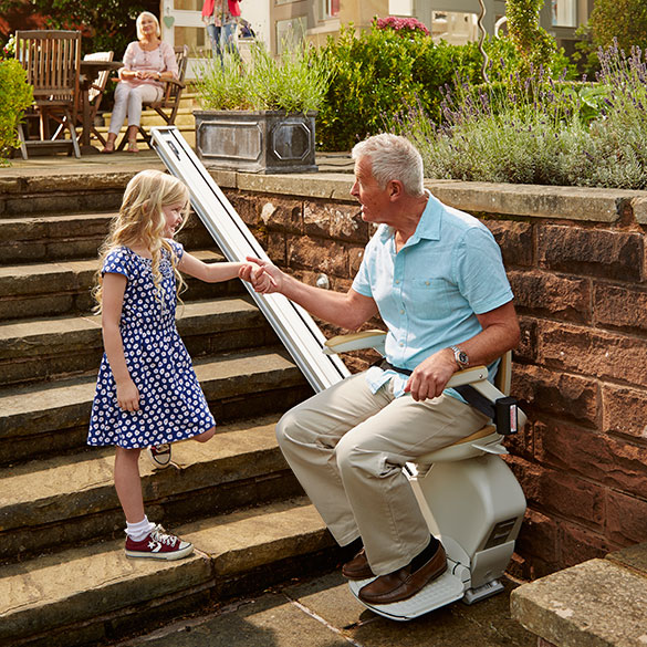 older man sits on outdoor stairlift and holds little girl's hand