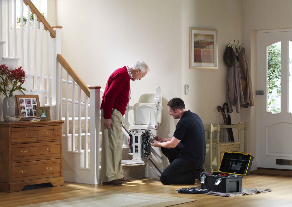 elderly man observes service technician changing battery on his stairlift